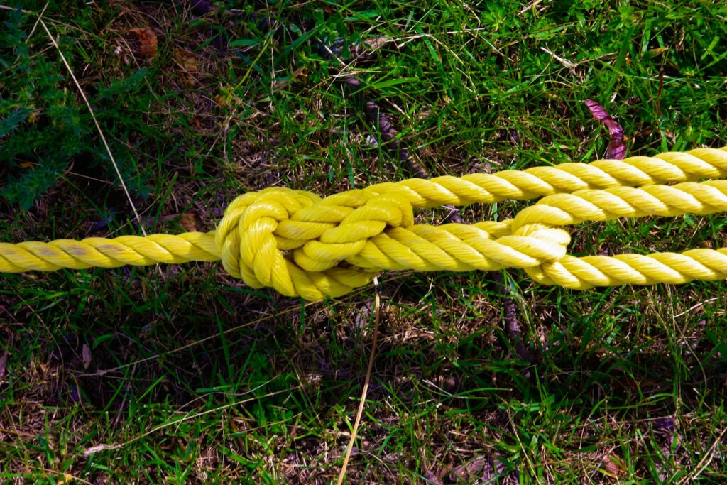 Hands tying a camping knot with rope beside outdoor gear at a campsite
