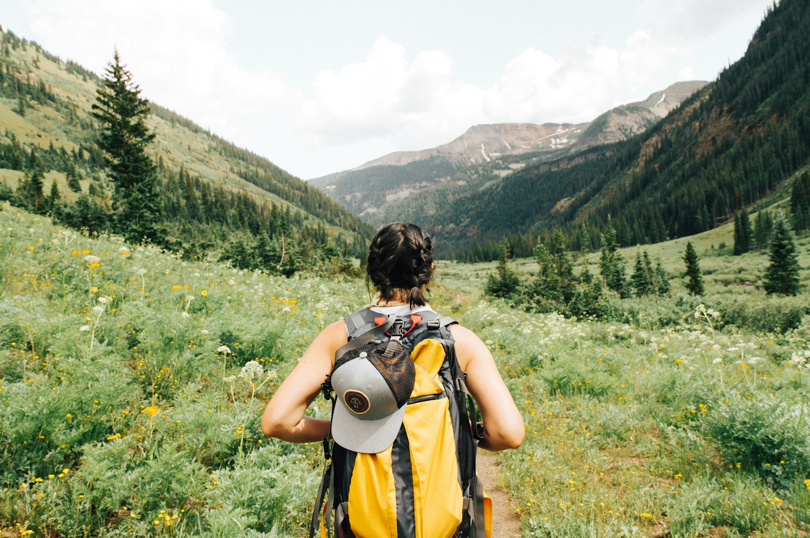 Hiker wearing lightweight layers, trail shoes, and a daypack on a sunny mountain trail