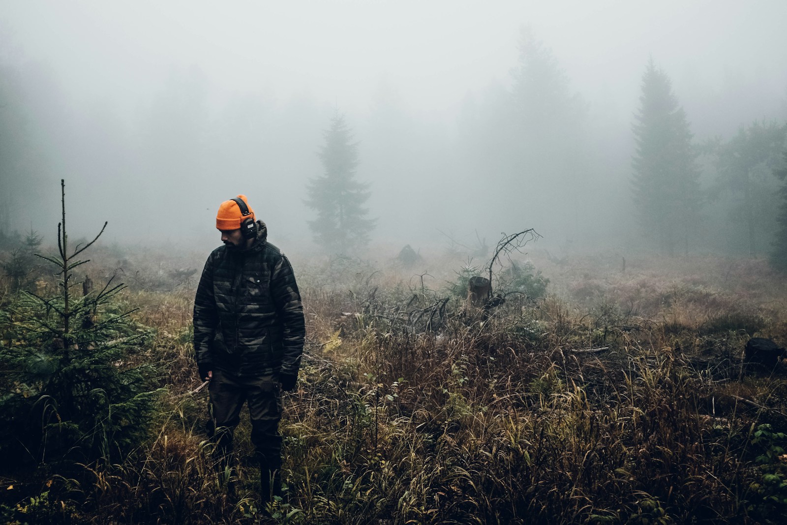 Hunter wearing layered outdoor clothing and blaze orange while walking through cool-season woods