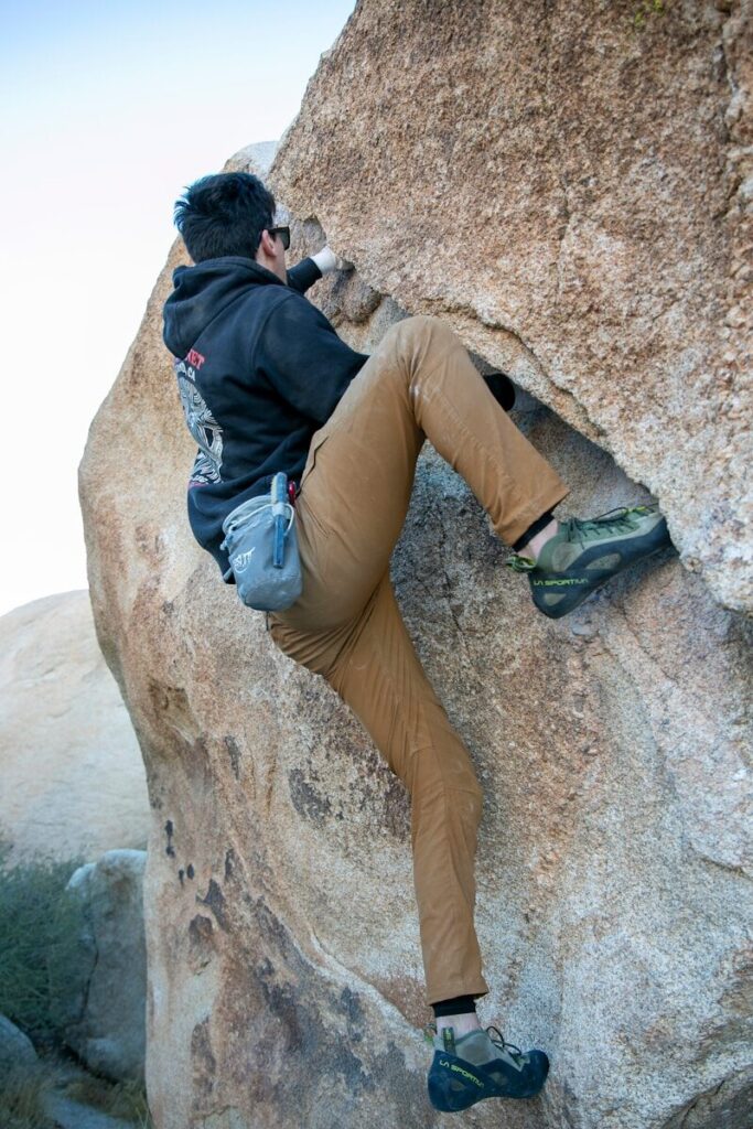 Rock climber wearing a helmet and harness on an outdoor cliff while a partner belays below