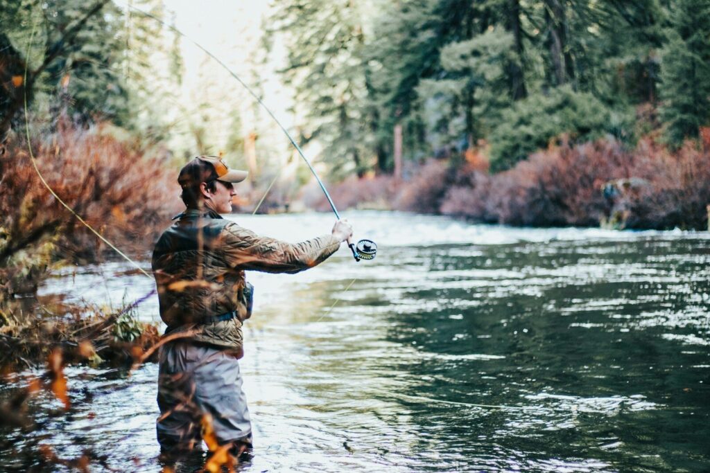 Fly angler wearing breathable waders, wading boots, sun shirt, and hat while standing in a clear river